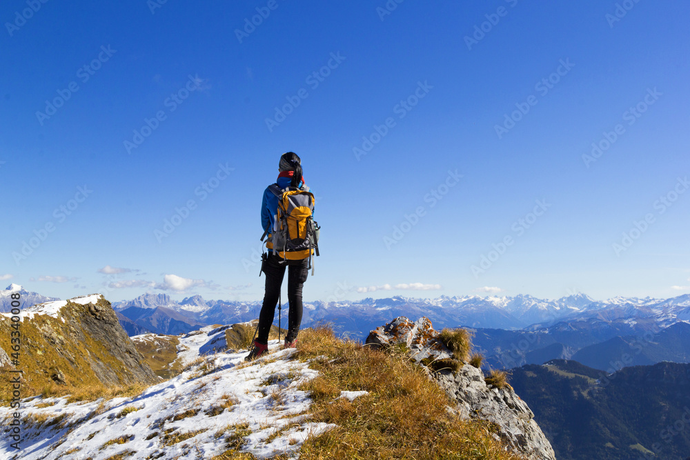 Backview of a woman hiker on the mountain top watching the Aips range under the blue sunny sky