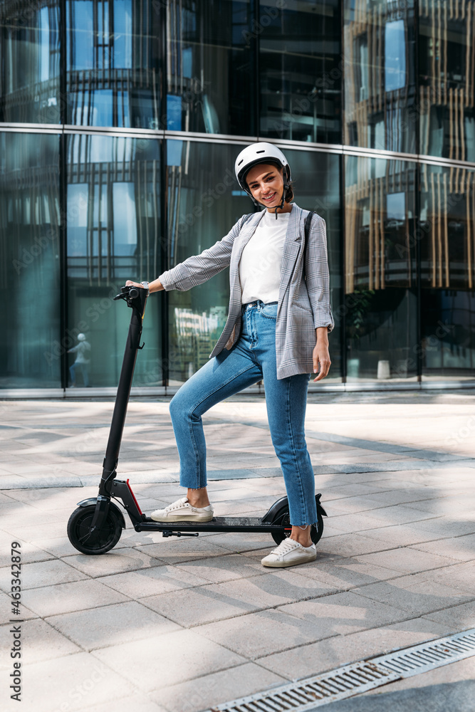 Young cheerful woman standing in the city with electric push scooter Young cheerful woman standing in the city with electric push scooter