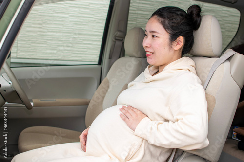 A young pregnant Asian woman sits on a passenger seat and cares her baby in her stomach © SaitoFAM