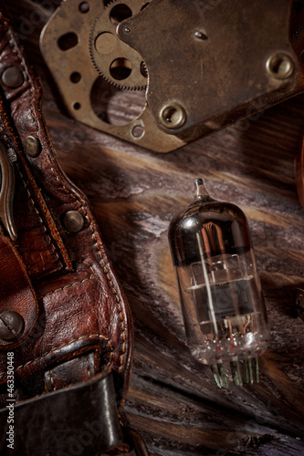 Steampunk still life - old vintage objects on a wooden background. Leather wrist watch, dark glasses, old tube lamps, magnifying glass, gears