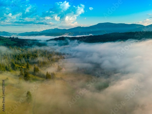 A thin morning fog covers the Ukrainian mountains. Green grass on the slopes of the mountains. A curly thin fog spreads over the mountains. Aerial drone view. photo
