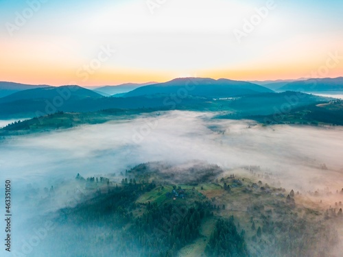 Fototapeta Naklejka Na Ścianę i Meble -  Fog spreads over the mountains at dawn. The sun rises on the horizon. Ukrainian Carpathians in the morning. Aerial drone view.
