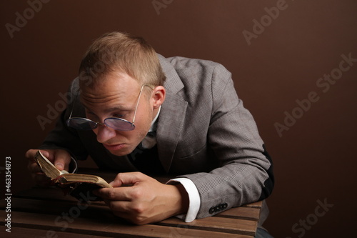 Portrait of a man.A comical, cheerful, cheerful guy in a suit and glasses, holding a book in his hands, carefully examines the book. High quality photo