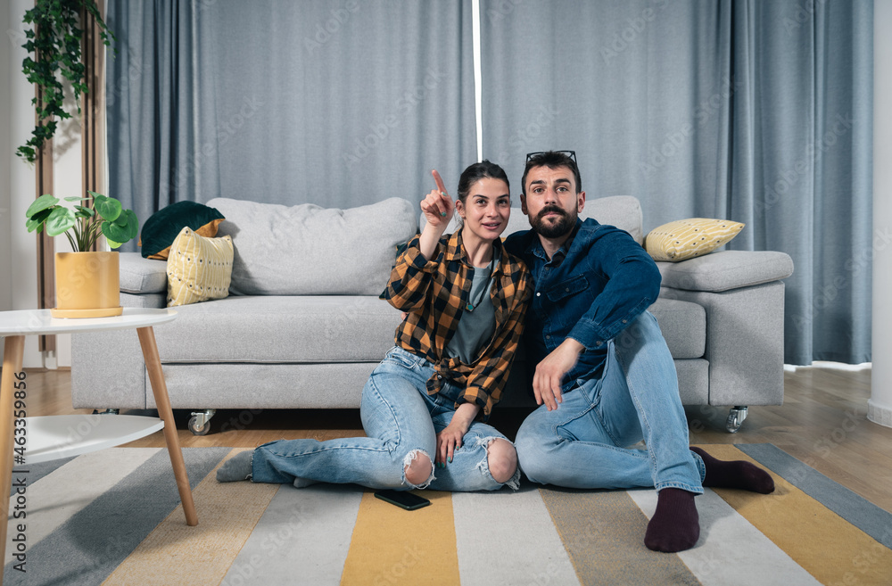 Naklejka premium Couple watch television show and man fake that he is interested while woman explaining to him who is who and what is the theme of that tv show, couple bonding concept