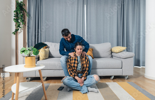Young couple in love a girl sitting on the floor and a guy on the couch and gently massages her neck muscle to relax her muscles after a hard day and to relieve her of stress, couple home massage 