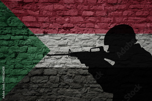 Soldier silhouette on the old brick wall with flag of sudan country. photo