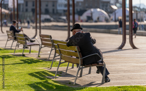 Hombre adulto irreconocible sentado en un banco frente al muelle en una mañana soleada