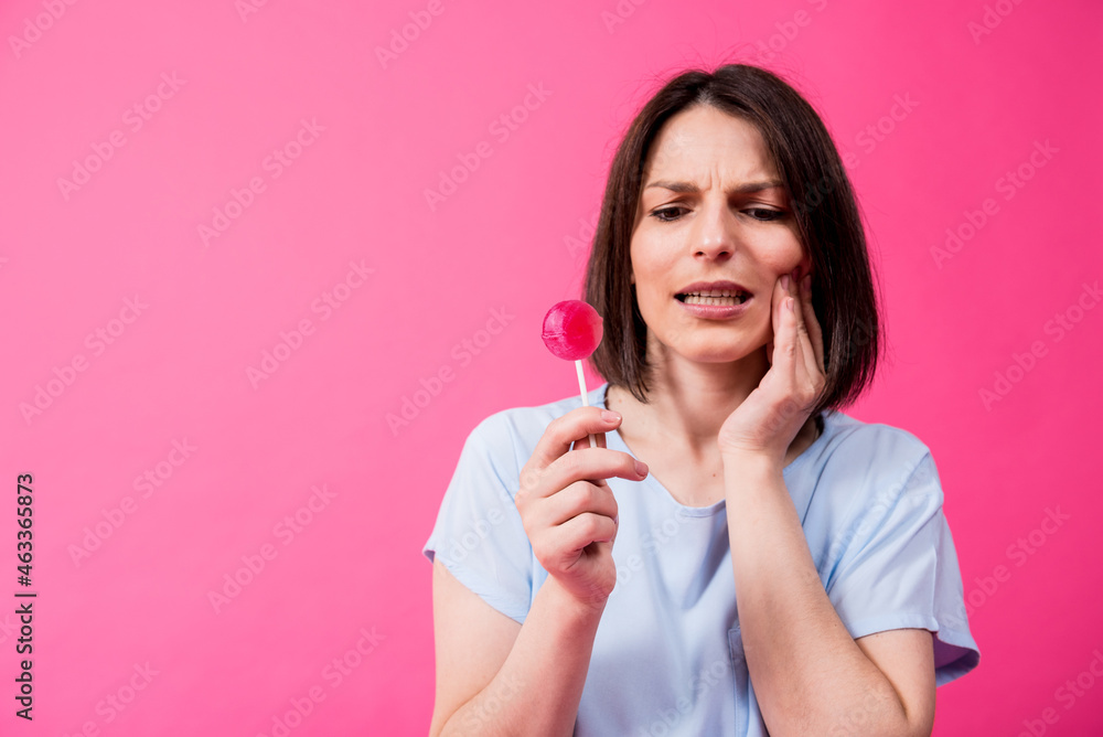 Young woman with sensitive teeth eating sweet lollipop on color background Young woman with sensitive teeth eating sweet lollipop on color background