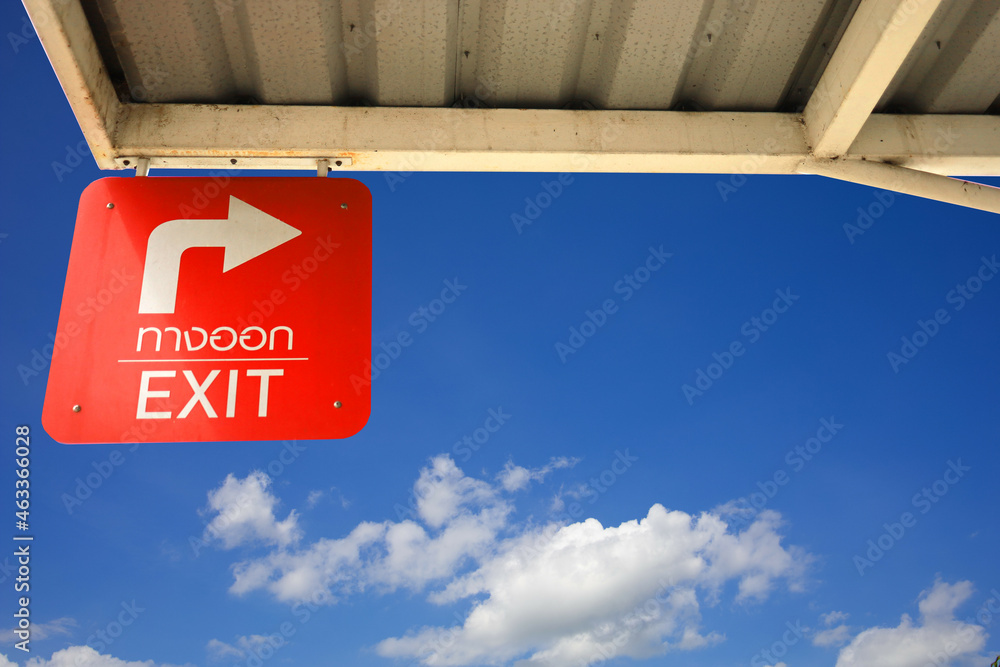 The red background exit sign with white letters under the blue sky and