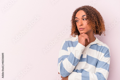 Young latin transsexual woman isolated on pink background looking sideways with doubtful and skeptical expression.