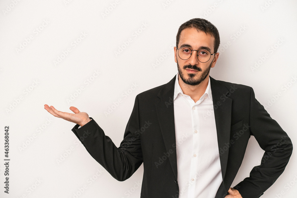 Young caucasian business man isolated on white background showing a copy space on a palm and holding another hand on waist.