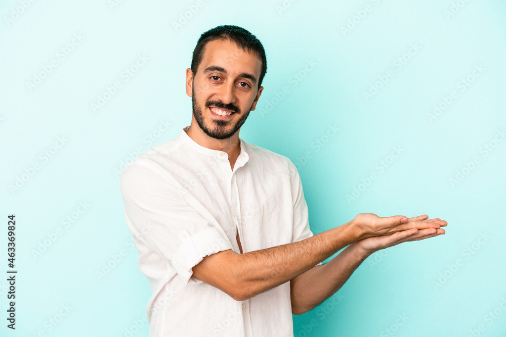 Young caucasian man isolated on blue background holding a copy space on a palm. Young caucasian man isolated on blue background holding a copy space on a palm.