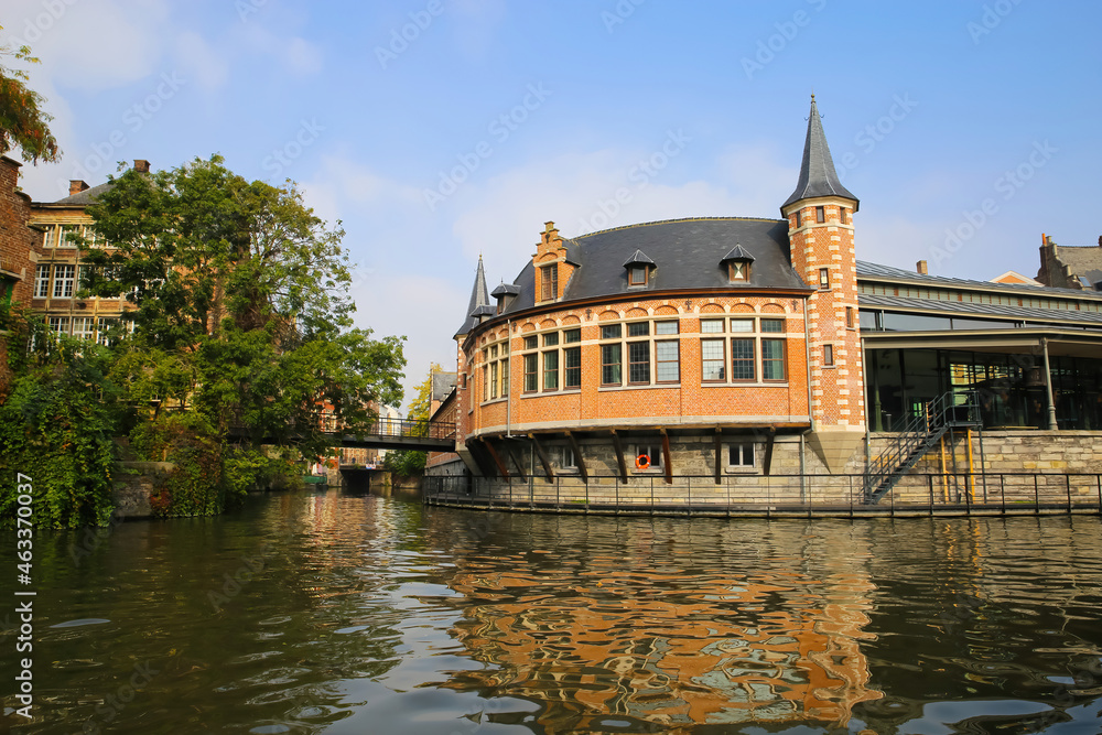 Obraz premium Ghent, Belgium - October 9. 2021: View over river Leie on tourist information center with green tree, bridge against blue morning sky