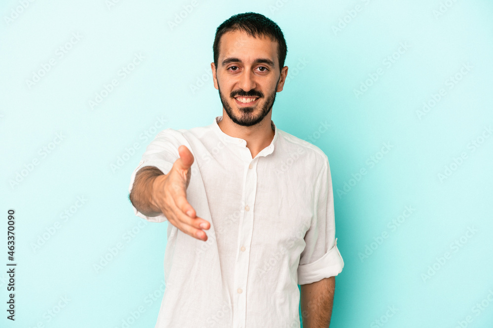 Young caucasian man isolated on blue background stretching hand at camera in greeting gesture. Young caucasian man isolated on blue background stretching hand at camera in greeting gesture.
