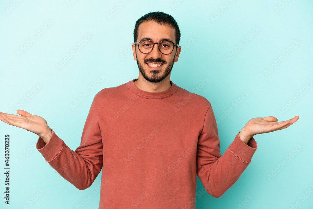 Young caucasian man isolated on blue background makes scale with arms, feels happy and confident. Young caucasian man isolated on blue background makes scale with arms, feels happy and confident.