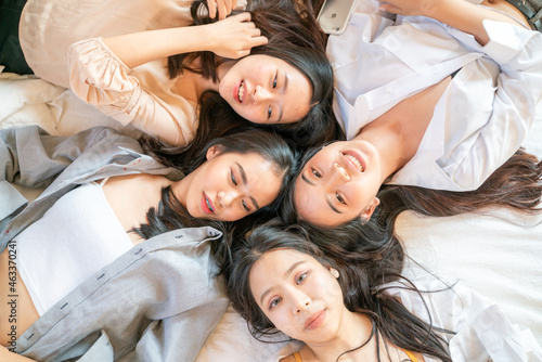 Group of beautiful asian women lying on cozy bed take photo with smartphone