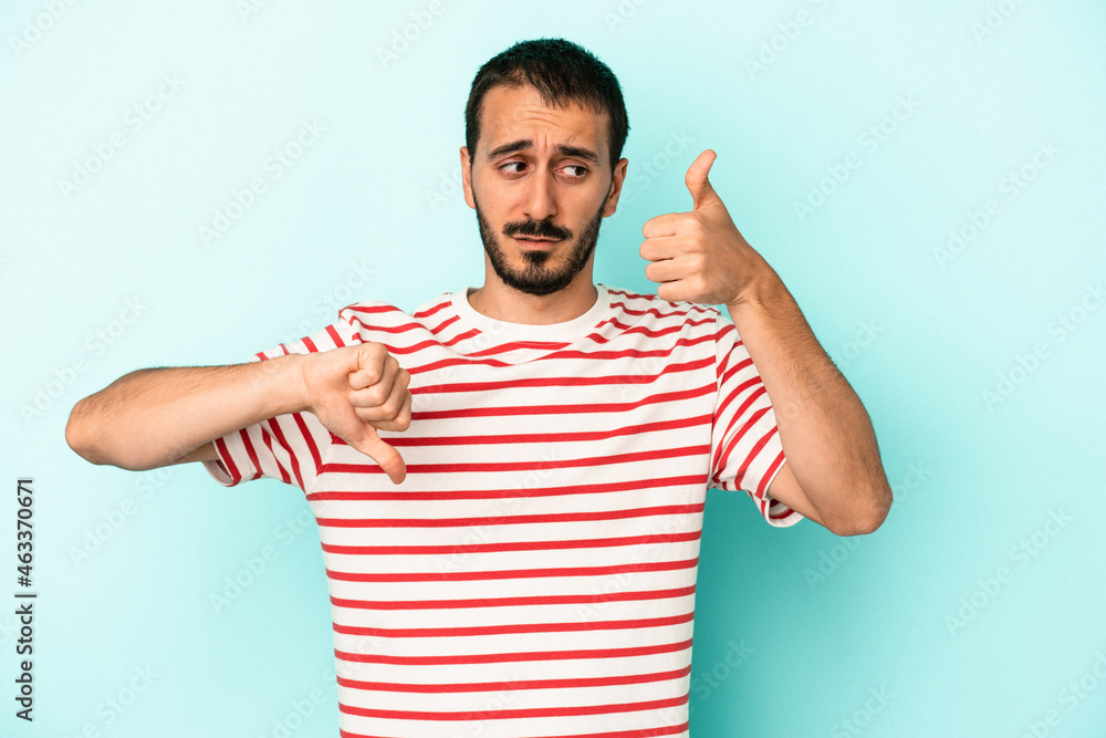 Young caucasian man isolated on blue background showing thumbs up and thumbs down, difficult choose concept Young caucasian man isolated on blue background showing thumbs up and thumbs down, difficult choose concept