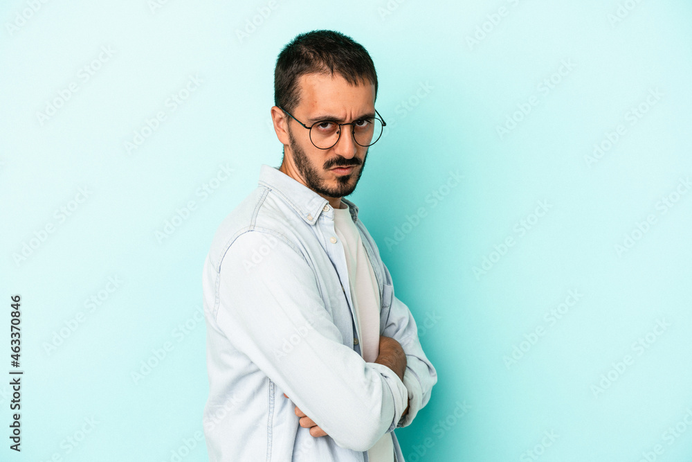 Young caucasian man isolated on blue background frowning face in displeasure, keeps arms folded. Young caucasian man isolated on blue background frowning face in displeasure, keeps arms folded.