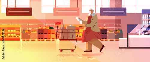 senior woman with full of products trolley cart checking shopping list in supermarket modern grocery shop interior