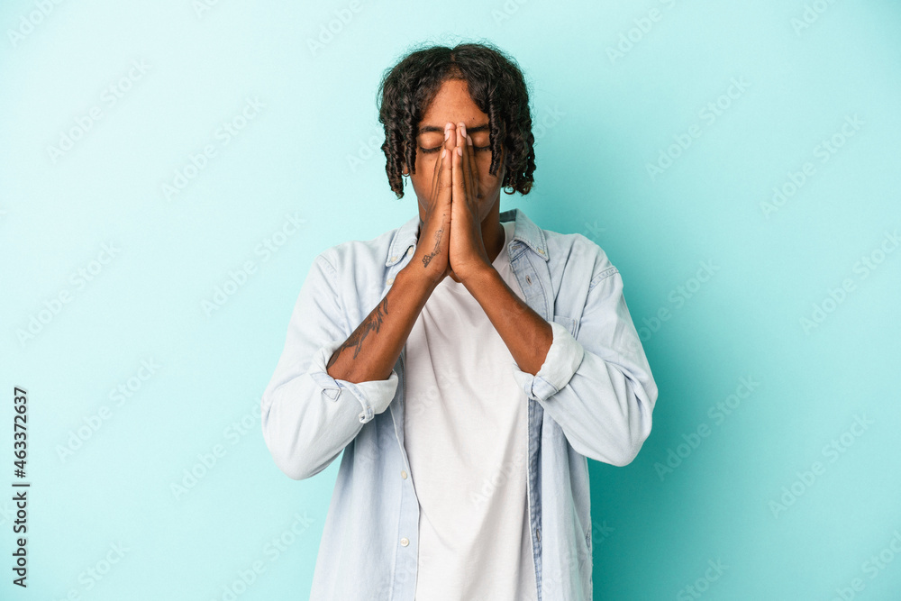 Young african american man isolated on blue background holding hands in pray near mouth, feels confident. Young african american man isolated on blue background holding hands in pray near mouth, feels confident.