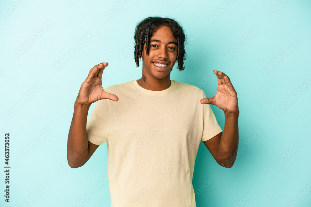 Young african american man isolated on blue background holding something with palms, offering to camera. Young african american man isolated on blue background holding something with palms, offering to camera.