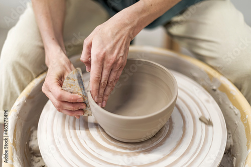 Hands of young woman working on pottery wheel in cozy workshop and making vase or mug