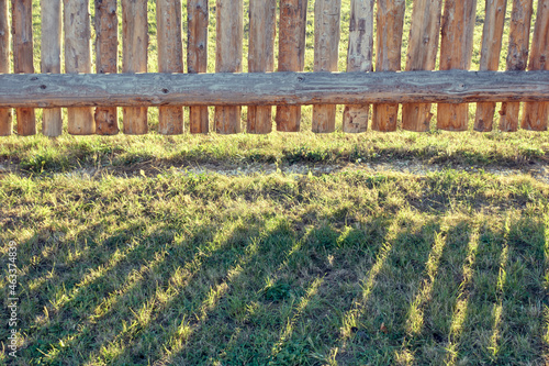 Shadow on the grass from a log fence. Rural fence in the rays of the setting sun. photo