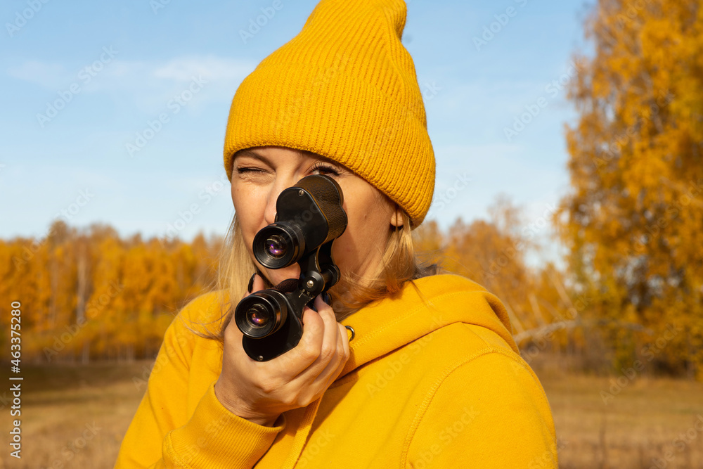 Obraz premium A beautiful positive woman in yellow clothes with binoculars on a picnic in the woods on an autumn day. The concept of the road, freedom, rest, travel