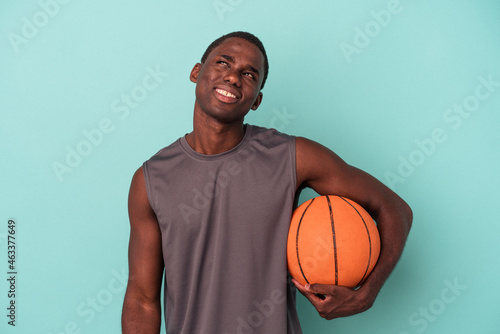 Young African American man playing basketball isolated on blue background dreaming of achieving goals and purposes © Asier