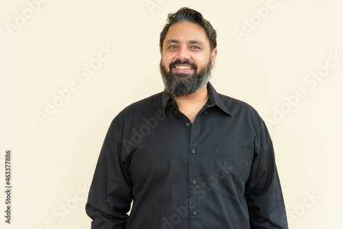 Plus size handsome bearded Indian man against plain background