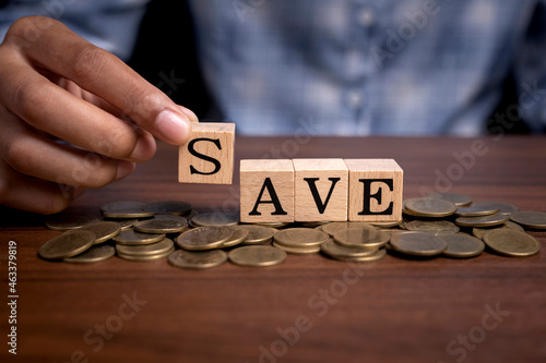 Woman hand holding wooden cube text "save" on pile of coins, money saving concept.