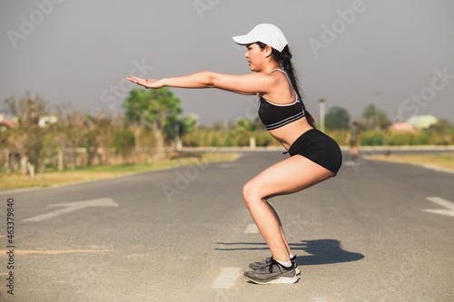 Image of fitness Asian woman 30s working out and stretching arms while standing on road in the morning at park.