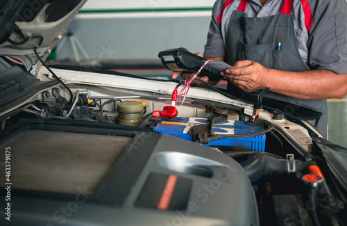 Automobile mechanic repairman hands checking car battery with modern tools digital multimeter in car service center.