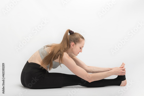 Stretching exercises. Young woman practices yoga on white background. Girl is engaged in gymnastics.