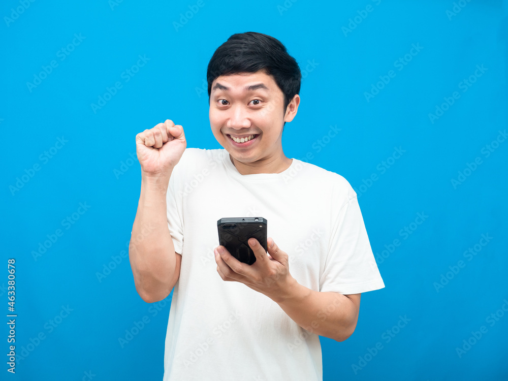 Man holding cellphone gesture happy show fist up blue background Man holding cellphone gesture happy show fist up blue background