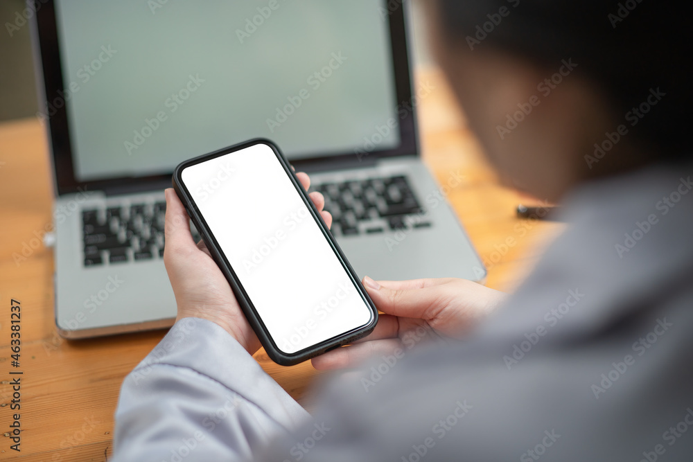 Woman holding mobile phone with white screen while sitting at her office desk.