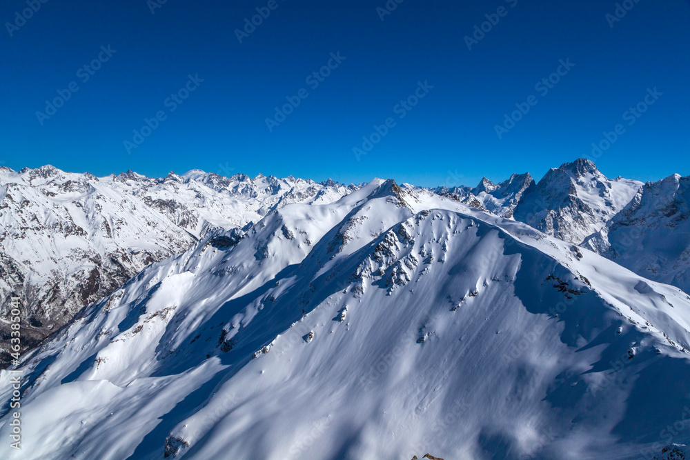 Obraz premium Caucasus Mountains, Panoramic view of the ski slope with the mountains Belalakaya, Sofrudzhu and Sulakhat on the horizon in winter day. Dombai ski resort, Western Caucasus, Karachai-Cherkess, Russia.