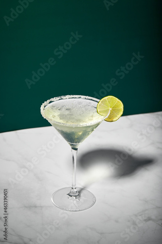 Martini cocktail with ice and slice of lime on marble table background. Alcoholic cocktail or non-alcoholic mocktail.