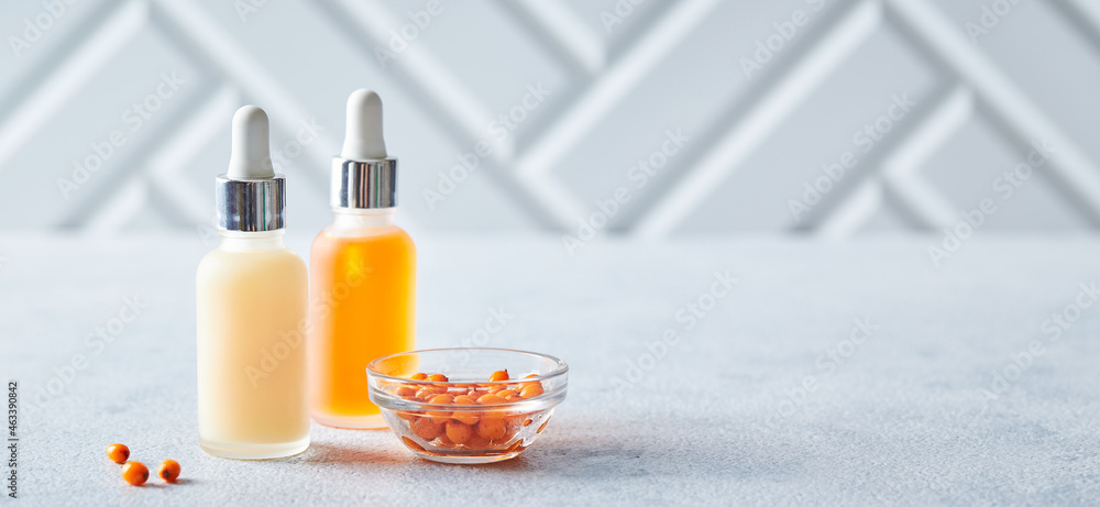 Glass bottles with seabackthorn face or body skin care products on light background. Self-care, cosmetics, beauty practices, self-care concept