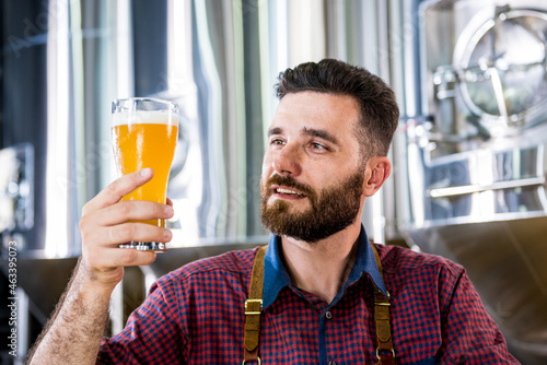 Young brewer wearing a leather apron is testing beer at a modern brewery