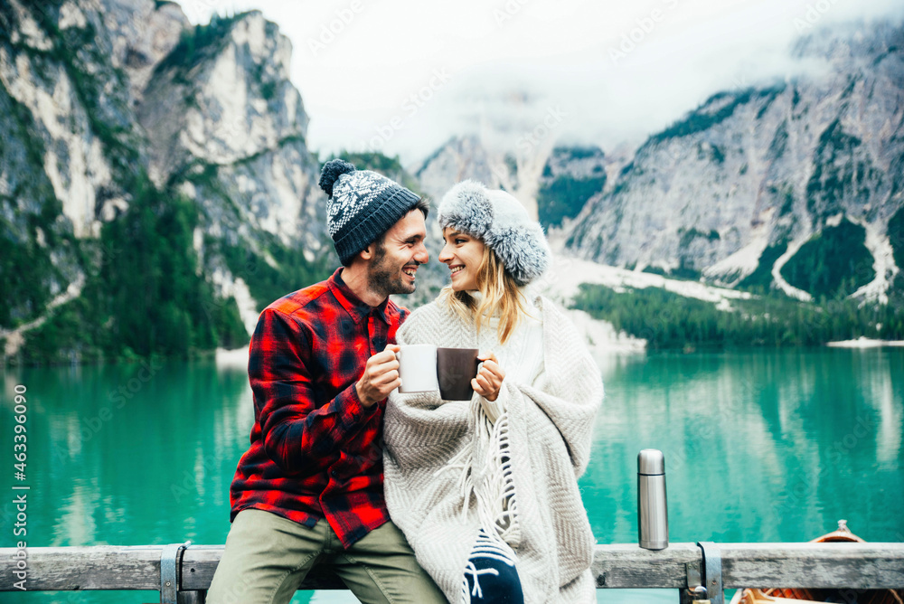 Portrait of a romantic couple of adults visiting an alpine lake at Braies Italy at winter - Tourist in love drinking hot coffee at mountains - Couple, wanderlust and travel concept.