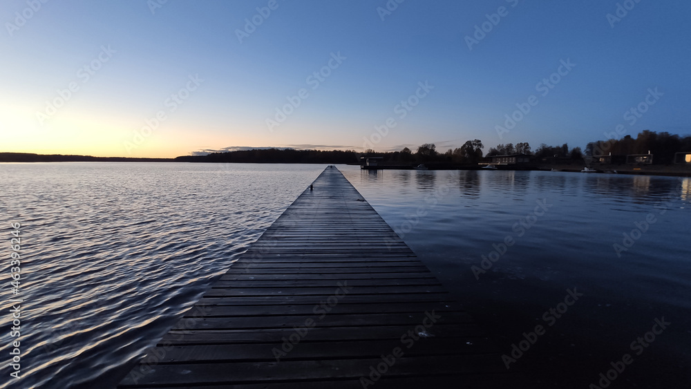 Wet wooden pier over Volga river matching dark blue color with the water pointing to the horizon lighten by the setting sun in the evening 
