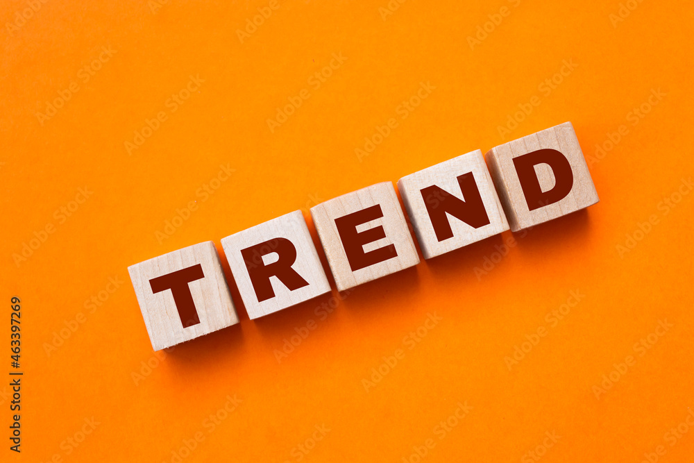 Obraz premium The hand puts a wooden cube with the letter T from the word TREND. The word is written on wooden cubes standing on the yellow surface of the table. Concept.