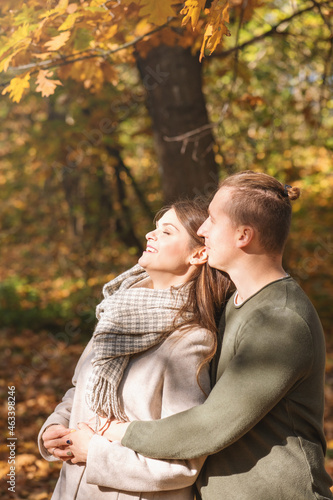 Leisure, relationship, nature concept. Man hugging girl and enjoy autumn sunlight under oak tree with yellow leaves. Bright vivid backlight filter. Girl face is in camera focus