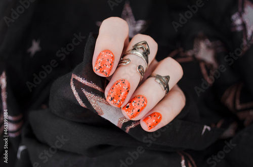 Orange matte nails on black blurry star background. Halloween nail art.
