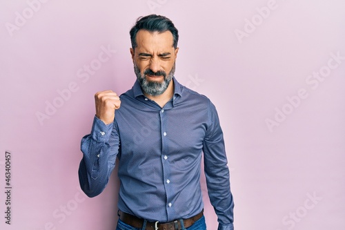 Middle age man with beard and grey hair wearing business clothes angry and mad raising fist frustrated and furious while shouting with anger. rage and aggressive concept.