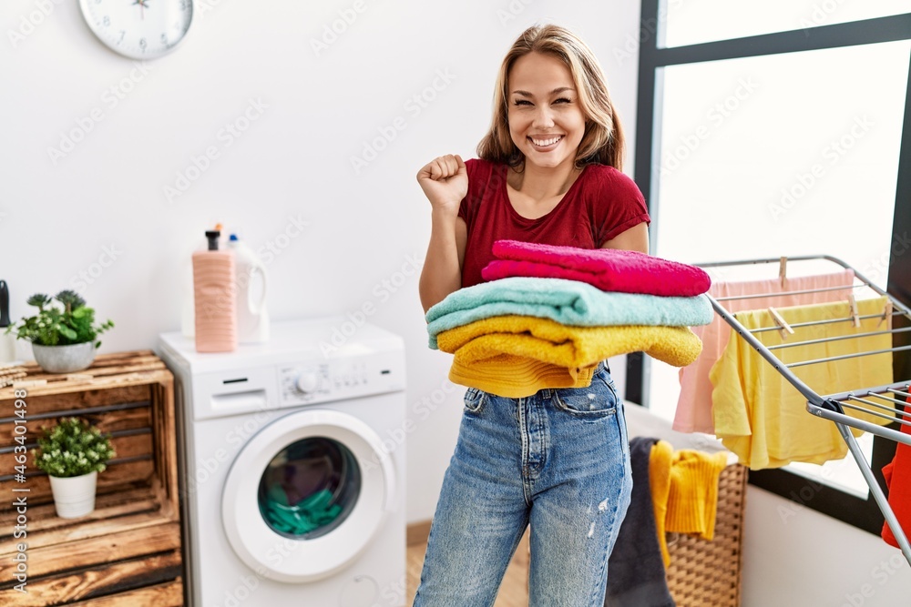 Young caucasian woman holding clean laundry screaming proud, celebrating victory and success very excited with raised arm Young caucasian woman holding clean laundry screaming proud, celebrating victory and success very excited with raised arm