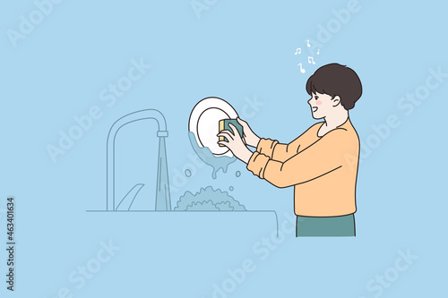 Obraz na plátně Small boy helper do housework wash dishes in kitchen singing having fun