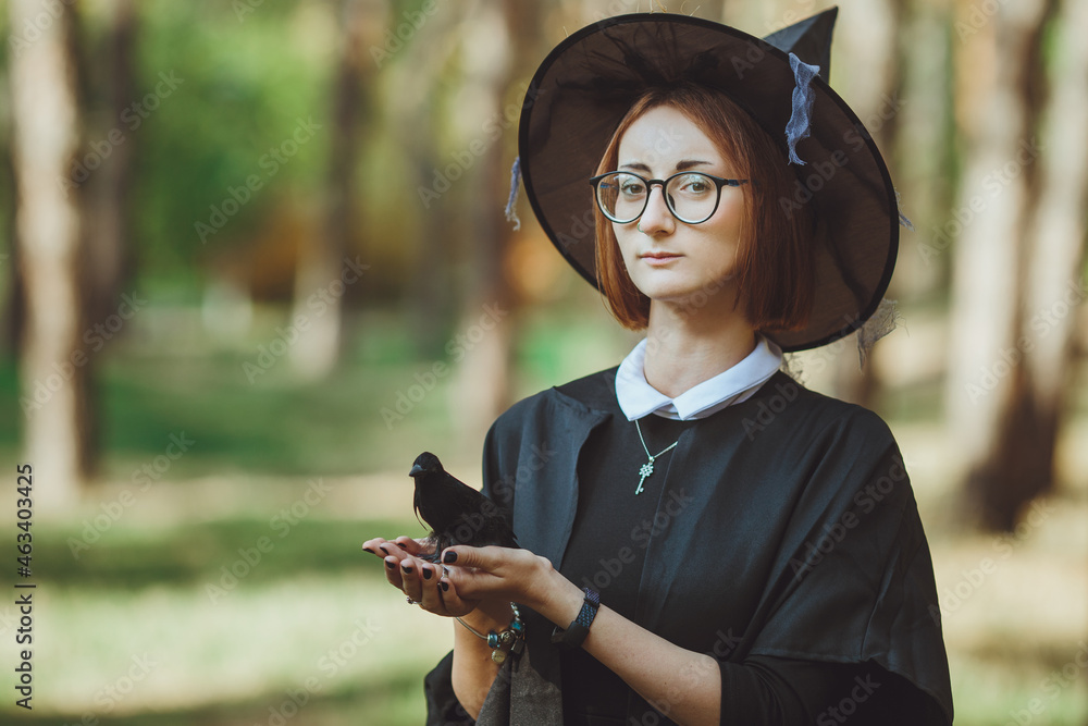 Halloween witch. Portrait of a girl in a hat and witch costume and with a black raven in the forest. Ready for the holiday wallet or life
