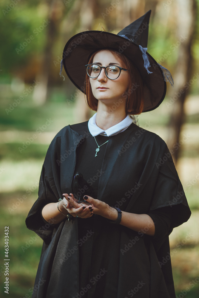 Halloween witch. Portrait of a girl in a hat and witch costume and with a black raven in the forest. Ready for the holiday wallet or life